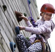 smiling girl in red helmet looking down form climbing wall
