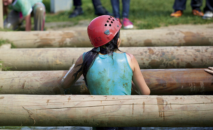girl climbing over poles on obstacle course