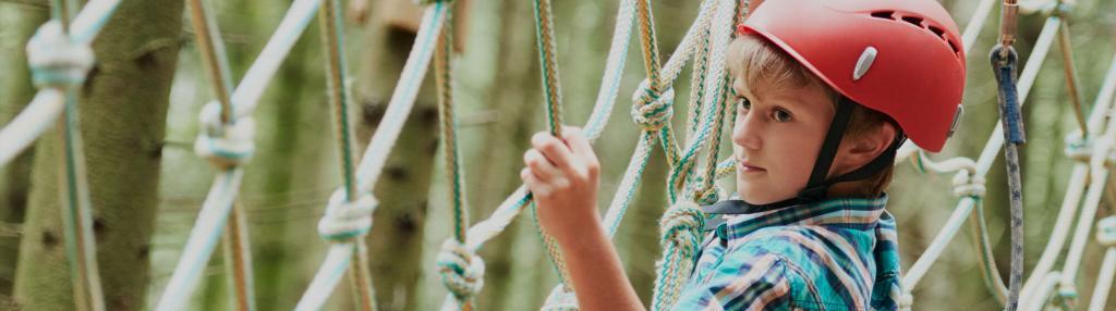 boy in red helmet climbing along a cargo net