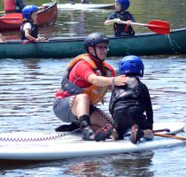 instructor helping child onto paddle board