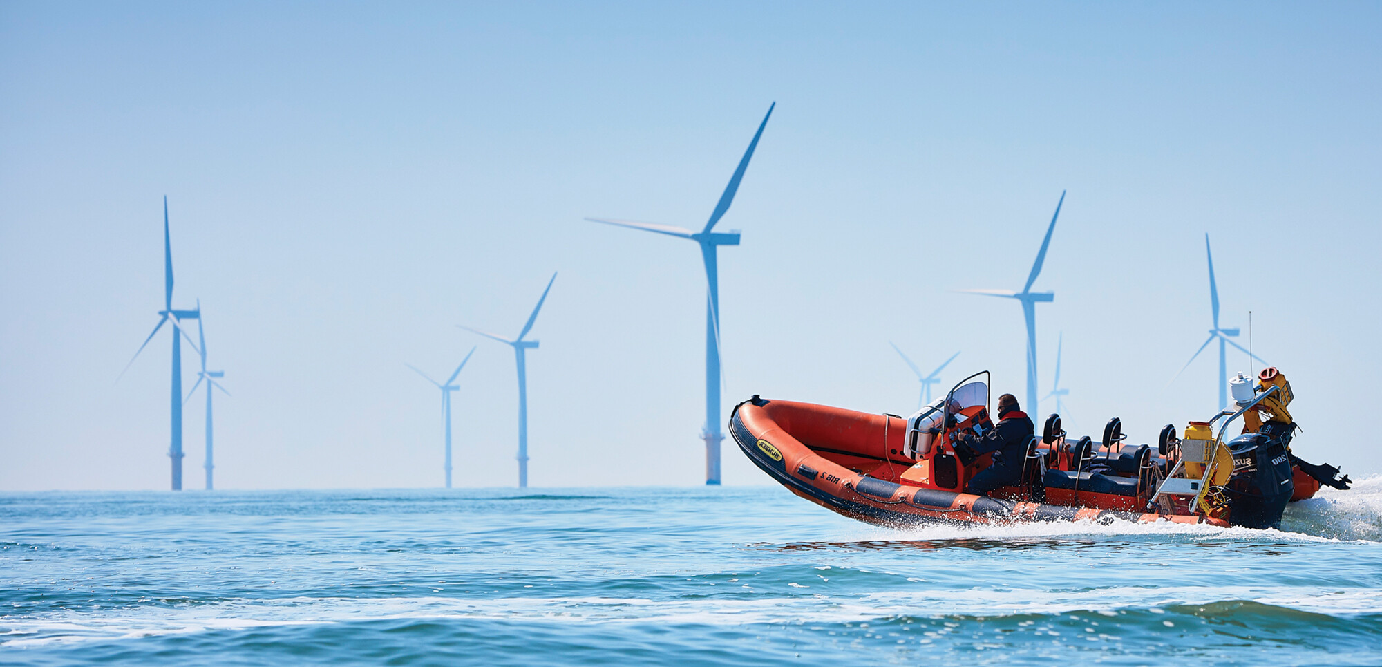 commercial powerboat on calm sea with wind farm in background