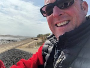 man in sunglasses smiling with beach in background