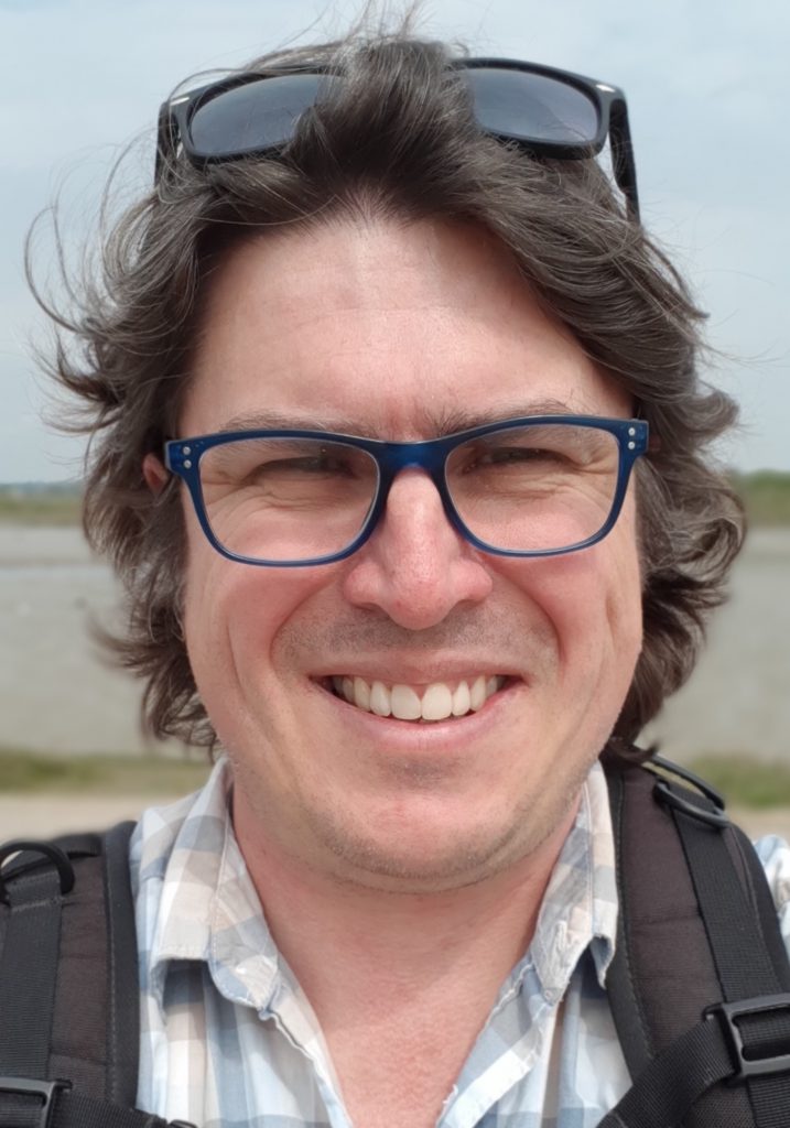 smiling man with brown hair and blue rim glasses