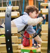 Young person with Curley Brown hair crawling through a section of Harlow High Ropes Adventure.