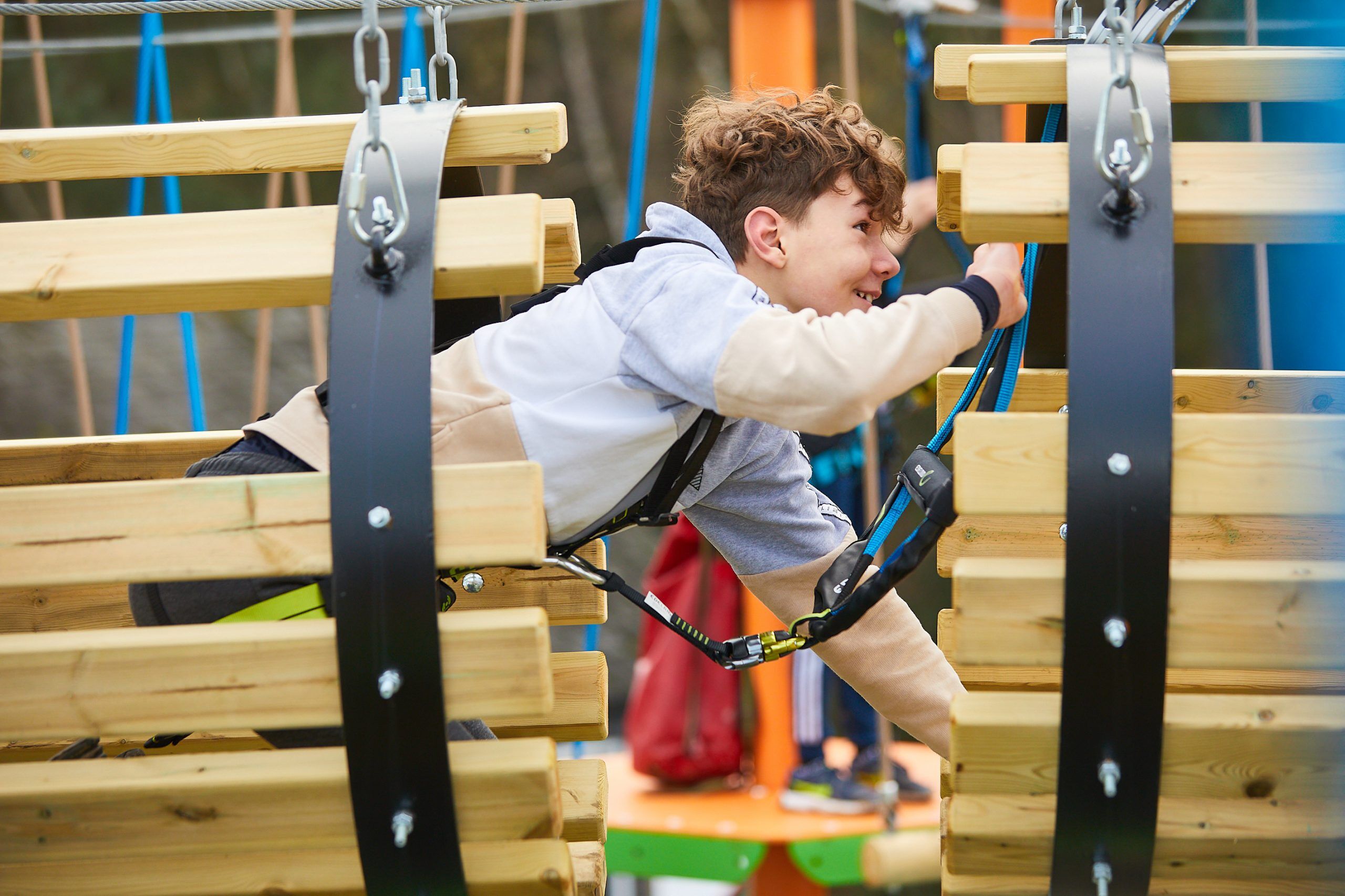 Young person with Curley Brown hair crawling through a section of Harlow High Ropes Adventure.