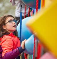 Young person with long brown hair and glasses concentrating on climbing the Harlow High Adventure clip and climb wall.