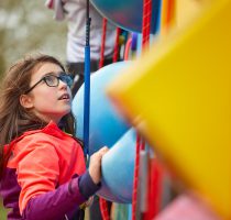 Young person with long brown hair and glasses concentrating on climbing the Harlow High Adventure clip and climb wall.