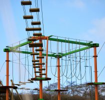 Harlow High Ropes Adventure course empty on a clear blue sky morning. The colourful orange and green metal with exciting obstacles hanging between them.