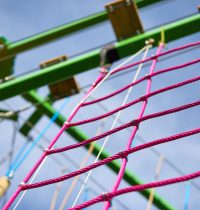 Pink square climbing net attached to bright green structure of the Harlow High Ropes Adventure course.