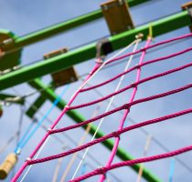 Pink square climbing net attached to bright green structure of the Harlow High Ropes Adventure course.