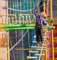 Young person reaching up to clip on safety harness to the next stage of Harlow High Ropes Adventure